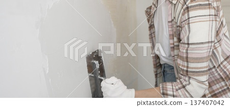 Unknown female construction worker wearing protective gloves applying plaster, smoothing wall surface during home renovation work 137407042