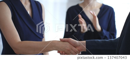 Business executives shaking hands during a successful corporate meeting, finalizing an important deal while a colleague claps in approval, symbolizing strong teamwork and growing success 137407043