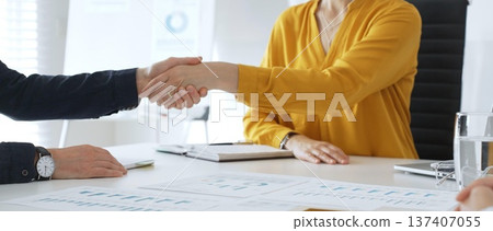 Professional businesspeople shaking hands, confirming partnership agreement in contemporary corporate workspace 137407055