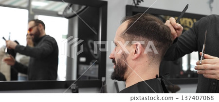 Skilled barber working on male client's hairstyle, carefully combing and preparing precision cut in contemporary barbershop setting Skilled barber working on male client's hairstyle, carefully combing and preparing precision cut in contemporary barbershop setting 137407068