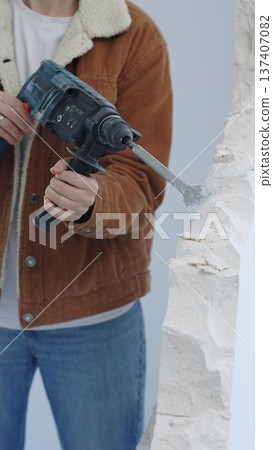 Unknown female construction worker demolishing concrete wall with rotary hammer, wearing protective safety gear. Renovation concept, closeup vertical view 137407082