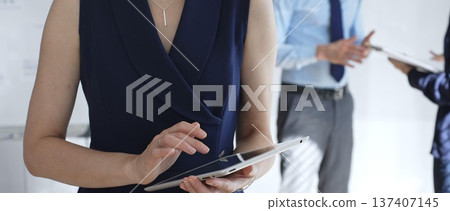 Professional businesswoman using a digital tablet in a modern office, interacting with a touchscreen while blurred colleagues collaborate in the background, focusing on tech and teamwork Professional businesswoman using a digital tablet in a modern office, interacting with a touchscreen while blurred colleagues collaborate in the background, focusing on tech and teamwork 137407145