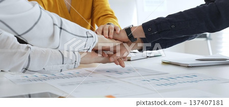 Business people team joining hands over workplace documents, symbolizing collaborative spirit and shared workplace success, close up view, casual style Business people team joining hands over workplace documents, symbolizing collaborative spirit and shared workplace success, close up view, casual style 137407181