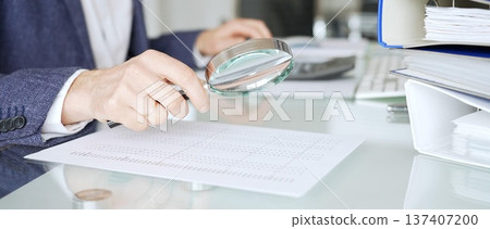 Auditor analyzing financial data with magnifying glass, scrutinizing business documents and accounting reports in office. Audit and taxes in business 137407200