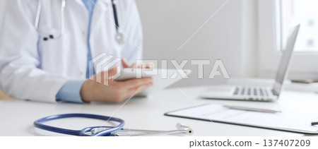 Closeup of blue stethoscope is lying on the table near female doctor reviewing prescription on digital tablet, representing digital healthcare workflow in contemporary medical setting. Medicine Closeup of blue stethoscope is lying on the table near female doctor reviewing prescription on digital tablet, representing digital healthcare workflow in contemporary medical setting. Medicine 137407209