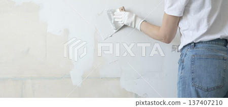 Unknown female construction worker applying plaster with putty knife, smoothing wall surface during home renovation, fixing wall imperfections with professional drywall repair technique, close up 137407210