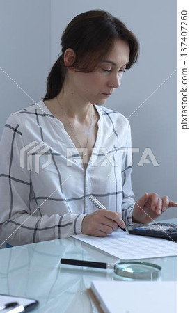 Female professional calculating finances, reviewing paperwork, tracking business expenses with precision and focus. Audit and taxes in business 137407260