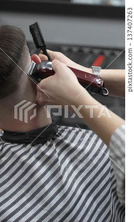 Professional barber grooming client's hair using electric clipper, delivering precise cut with skill in contemporary salon setting, close-up view Professional barber grooming client's hair using electric clipper, delivering precise cut with skill in contemporary salon setting, close-up view 137407263