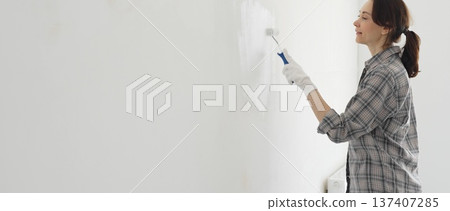 Woman wearing white gloves painting white wall with paint roller, experiencing home renovation and transforming living space Woman wearing white gloves painting white wall with paint roller, experiencing home renovation and transforming living space 137407285