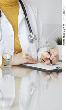 Female physician or medic completing paperwork, preparing a diagnosis, or providing healthcare service in a clean modern office. Medicine, healthcare and science concept Female physician or medic completing paperwork, preparing a diagnosis, or providing healthcare service in a clean modern office. Medicine, healthcare and science concept 137407306