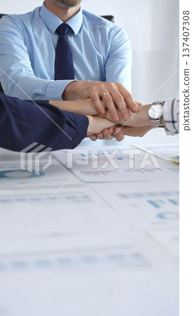 Teamwork and business collaboration with colleagues joining hands over financial charts, symbolizing unity, partnership, success, and strategic corporate planning 137407308