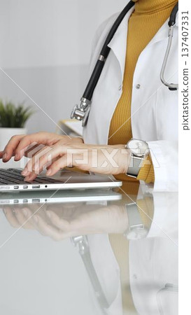 Female doctor working on laptop, managing patient data, writing prescriptions in clinic and filling out patient medical records. Concept of medicine, healthcare and science 137407331