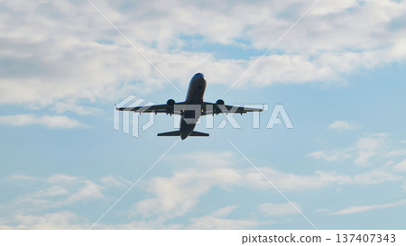 Commercial passenger airplane taking off and ascending into a blue cloudy sky, low angle view. Commercial passenger airplane taking off and ascending into a blue cloudy sky, low angle view. 137407343