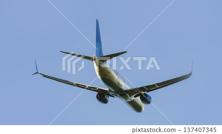 Commercial passenger jet airplane taking off, ascending into a clear blue sky. Low angle view from below. Commercial passenger jet airplane taking off, ascending into a clear blue sky. Low angle view from below. 137407345