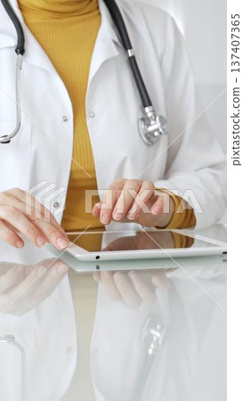 Doctor using tablet, working in clinic office, health care professional analyzing electronic medical records data. Medicine, healthcare and science concept 137407365