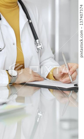 Female physician or medic completing paperwork, preparing a diagnosis, or providing healthcare service in a clean modern office. Medicine, healthcare and science concept 137407374