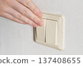 Hand pressing light switch on white wall, controlling power 137408655