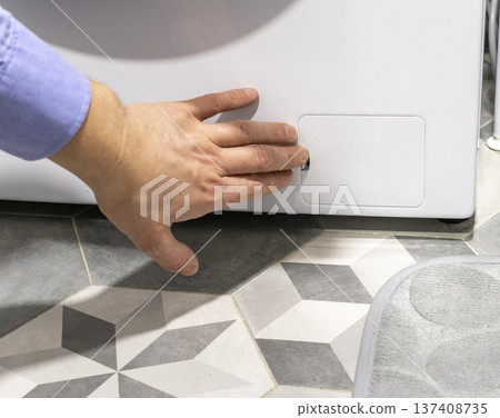 Man opening the drain pump filter access panel of the front loading washing machine 137408735