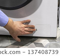 Man opening the drain pump filter access panel of the front loading washing machine 137408739