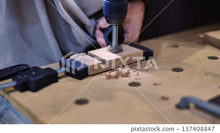 Woodworking project in progress, drilling a hole into wooden workpiece fixed with clamps 137408847