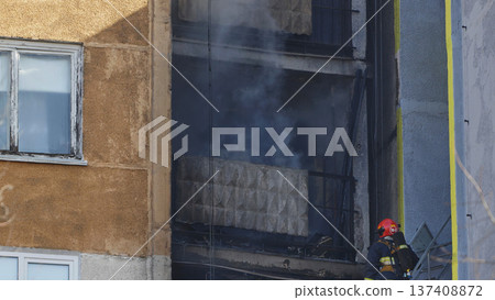 Firefighter checking burning building during an apartment fire, smoke coming from windows 137408872