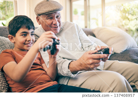 Family, fun and a boy gaming with his grandfather on a sofa in the living room of their home during a visit. Video game, children and a senior man learning how to play from his gamer grandson Family, fun and a boy gaming with his grandfather on a sofa in the living room of their home during a visit. Video game, children and a senior man learning how to play from his gamer grandson 137408957