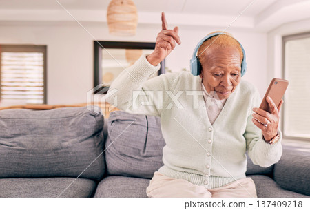 Headphones, dancing and senior woman on sofa in home relax and listen to music, audio and radio. Retirement, fun and happy person in living room on phone for streaming track, song and subscription Headphones, dancing and senior woman on sofa in home relax and listen to music, audio and radio. Retirement, fun and happy person in living room on phone for streaming track, song and subscription 137409218