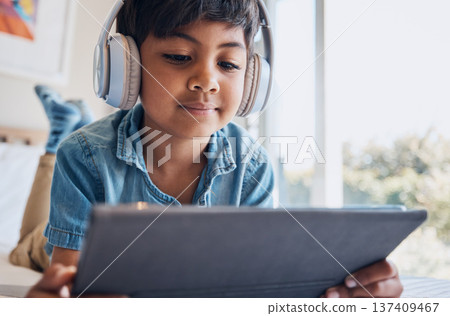 Boy kid, tablet and headphones on bed, reading or idea with e learninng, movie and relax with web video. Male child, digital touchscreen and thinking in bedroom for audio, show and streaming in home 137409467