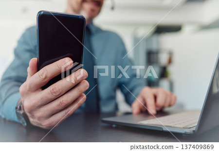 Businessman, hands and phone with laptop in communication, social media or networking at the office. Closeup of man working on computer and mobile smartphone technology in telemarketing at workplace Businessman, hands and phone with laptop in communication, social media or networking at the office. Closeup of man working on computer and mobile smartphone technology in telemarketing at workplace 137409869
