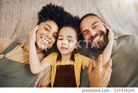 Portrait, family and a boy with his parents on the floor of the living room in their home together from above. Face, smile or love with an interracial mother, father and son lying down closeup 137410105