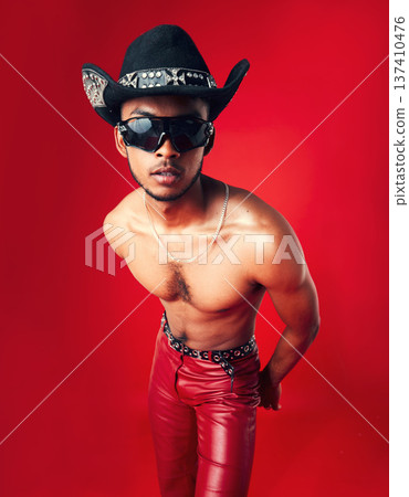 Fashion, man and cowboy in hat, shirtless with sunglasses and gen z isolated on red background. Confident model, cool and leather pants with eyewear accessory, western aesthetic and edgy in studio Fashion, man and cowboy in hat, shirtless with sunglasses and gen z isolated on red background. Confident model, cool and leather pants with eyewear accessory, western aesthetic and edgy in studio 137410476