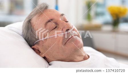 Oxygen, hospital bed and senior man sleeping with ventilation and breathing tube support in a clinic. Elderly patient, medical care and emergency room with male person at a doctor for healthcare Oxygen, hospital bed and senior man sleeping with ventilation and breathing tube support in a clinic. Elderly patient, medical care and emergency room with male person at a doctor for healthcare 137410720