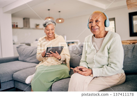 Headphones, relax and senior women on sofa in home listen to music, audio and radio with friend. Retirement, technology and people in living room on tablet for streaming track, song or subscription 137411178