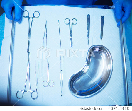 Surgery, tools and medical table in hospital, operation room and equipment with scalpel knife, scissors and metal bowl. Surgeon, hands and above doctor ready with medicine or tool for procedure Surgery, tools and medical table in hospital, operation room and equipment with scalpel knife, scissors and metal bowl. Surgeon, hands and above doctor ready with medicine or tool for procedure 137411468