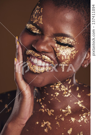 Black woman, silly face and gold makeup with luxury dermatology and skincare mask with glitter. Sparkle, smile and beauty with rich and shine of cosmetics and model in a studio with facial art Black woman, silly face and gold makeup with luxury dermatology and skincare mask with glitter. Sparkle, smile and beauty with rich and shine of cosmetics and model in a studio with facial art 137411894