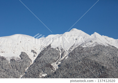 View of the mountains from Rosa Khutor, Krasnaya Polyana in winter. Snow-covered mountains against a blue sky. View of the mountains from Rosa Khutor, Krasnaya Polyana in winter. Snow-covered mountains against a blue sky. 137412020