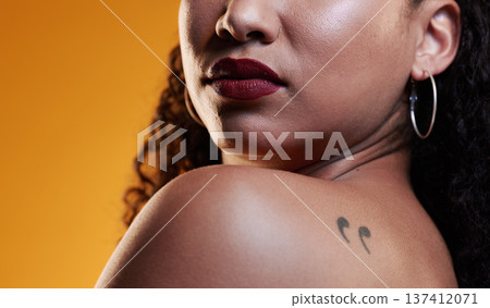 Beauty, makeup and a woman with a tattoo in studio for cosmetics, skin glow and dermatology. Closeup of a young female model on an orange background in studio with body art, confidence and comma ink 137412071