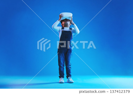 Glasses, virtual reality and metaverse with girl, online games or digital transformation on blue studio background. Kid, child and model with vr headset with technology, futuristic and live streaming Glasses, virtual reality and metaverse with girl, online games or digital transformation on blue studio background. Kid, child and model with vr headset with technology, futuristic and live streaming 137412379