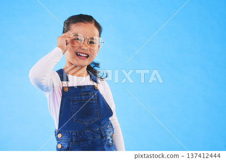 Girl child, glasses and frame in studio portrait for vision, health and eye care by blue background. Female kid, test spectacles and young fashion model with lens, smile or eyesight with mockup space 137412444
