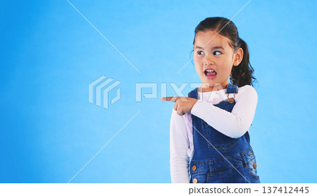 Pointing, blue background and girl with mockup space for sale, advertising and promotion. Emoji, happy and young child in studio with hand gesture for discount information, announcement and news 137412445