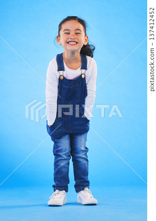 Excited girl child, fashion and studio portrait with jeans, dungaree and trendy style by blue background. Female kid model, smile and happy for clothes, aesthetic and youth culture by backdrop Excited girl child, fashion and studio portrait with jeans, dungaree and trendy style by blue background. Female kid model, smile and happy for clothes, aesthetic and youth culture by backdrop 137412452