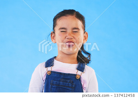 Funny, face of child and girl with silly, goofy or facial expression on blue background in studio with fashion for children. Kid, portrait and tongue out of mouth in joke, humor or emoji for comedy Funny, face of child and girl with silly, goofy or facial expression on blue background in studio with fashion for children. Kid, portrait and tongue out of mouth in joke, humor or emoji for comedy 137412458
