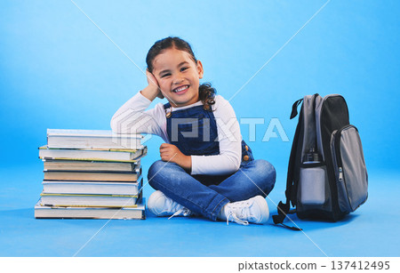 Girl child, sitting and books in studio portrait, backpack and excited for learning on floor by blue background. Female kid, education and development with smile, future and studying for knowledge Girl child, sitting and books in studio portrait, backpack and excited for learning on floor by blue background. Female kid, education and development with smile, future and studying for knowledge 137412495