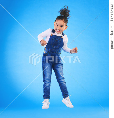 Happy, jumping and portrait of a child in a studio with excitement, joy or wow expression. Happiness, smile and full length of a girl kid model moving for good news isolated by a blue background. Happy, jumping and portrait of a child in a studio with excitement, joy or wow expression. Happiness, smile and full length of a girl kid model moving for good news isolated by a blue background. 137412538