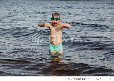 child happily excitedly enters water, swims, dives lake or pond on a hot, sunny summer day during vacation or school break. active healthy lifestyle. child wearing turquoise swimming trunks goggles. child happily excitedly enters water, swims, dives lake or pond on a hot, sunny summer day during vacation or school break. active healthy lifestyle. child wearing turquoise swimming trunks goggles. 137412907