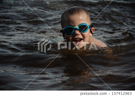 child happily excitedly enters water, swims, dives lake or pond on a hot, sunny summer day during vacation or school break. active healthy lifestyle. child wearing turquoise swimming trunks goggles. child happily excitedly enters water, swims, dives lake or pond on a hot, sunny summer day during vacation or school break. active healthy lifestyle. child wearing turquoise swimming trunks goggles. 137412963