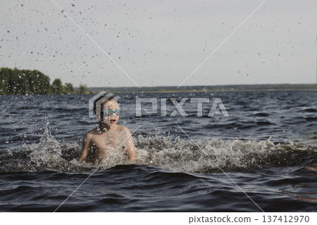 child happily excitedly enters water, swims, dives lake or pond on a hot, sunny summer day during vacation or school break. active healthy lifestyle. child wearing turquoise swimming trunks goggles. child happily excitedly enters water, swims, dives lake or pond on a hot, sunny summer day during vacation or school break. active healthy lifestyle. child wearing turquoise swimming trunks goggles. 137412970