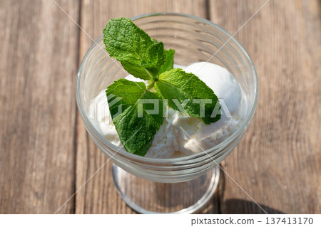 Delicious butter ice cream in a glass bowl with green mint on a wooden board, close-up. Delicious butter ice cream in a glass bowl with green mint on a wooden board, close-up. 137413170