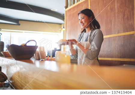 Chinese food, waitress and an asian woman in a sushi restaurant to serve a traditional meal for nutrition. Kitchen, smile and cooking with a happy young employee in an eatery for fine dining cuisine 137413404