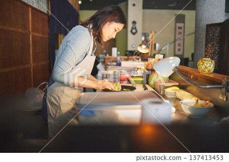 Chinese food, chef and an asian woman in a sushi restaurant to serve a traditional meal for nutrition. Kitchen, cooking or preparation with a happy young employee in an eatery for fine dining cuisine Chinese food, chef and an asian woman in a sushi restaurant to serve a traditional meal for nutrition. Kitchen, cooking or preparation with a happy young employee in an eatery for fine dining cuisine 137413453